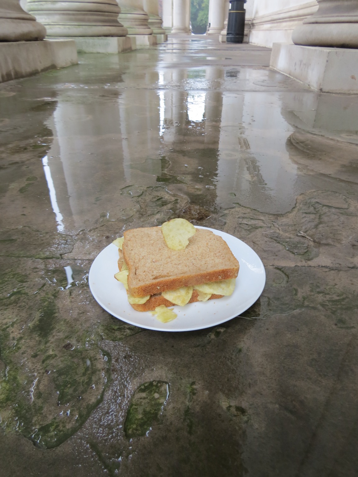 Crisp sandwich with crisp stuck in it on a wet stone floor
