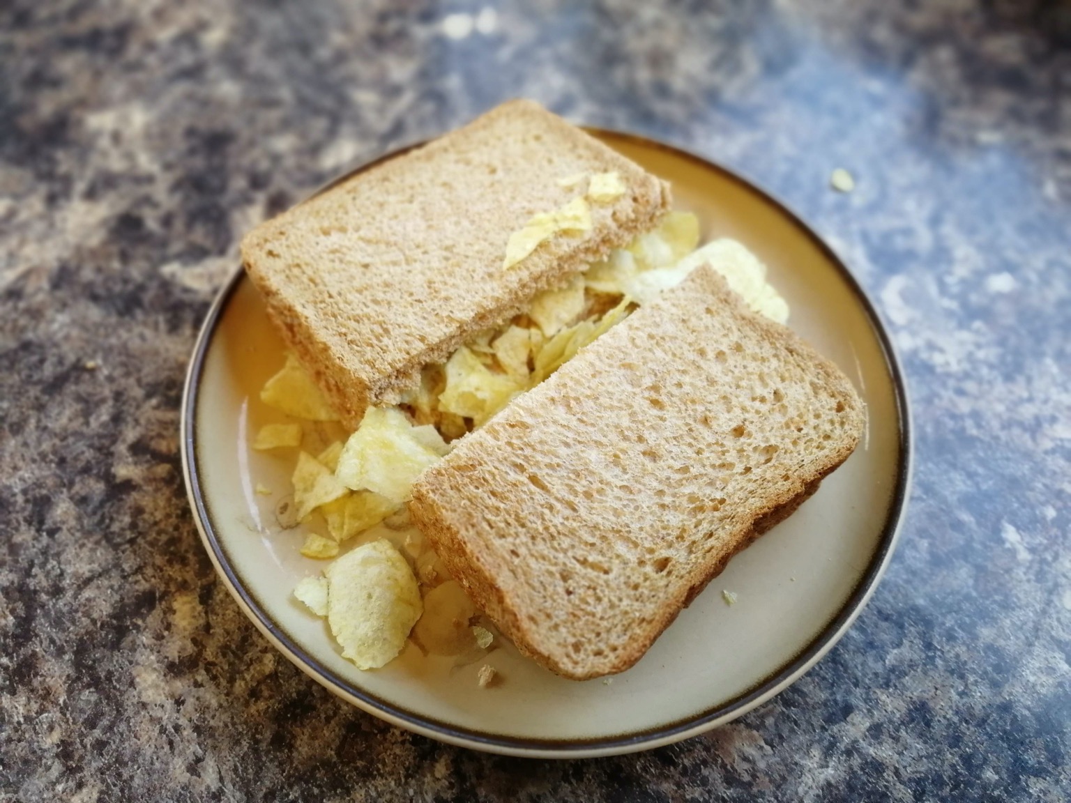 Halved brown bread sandwich over-filled with crisps