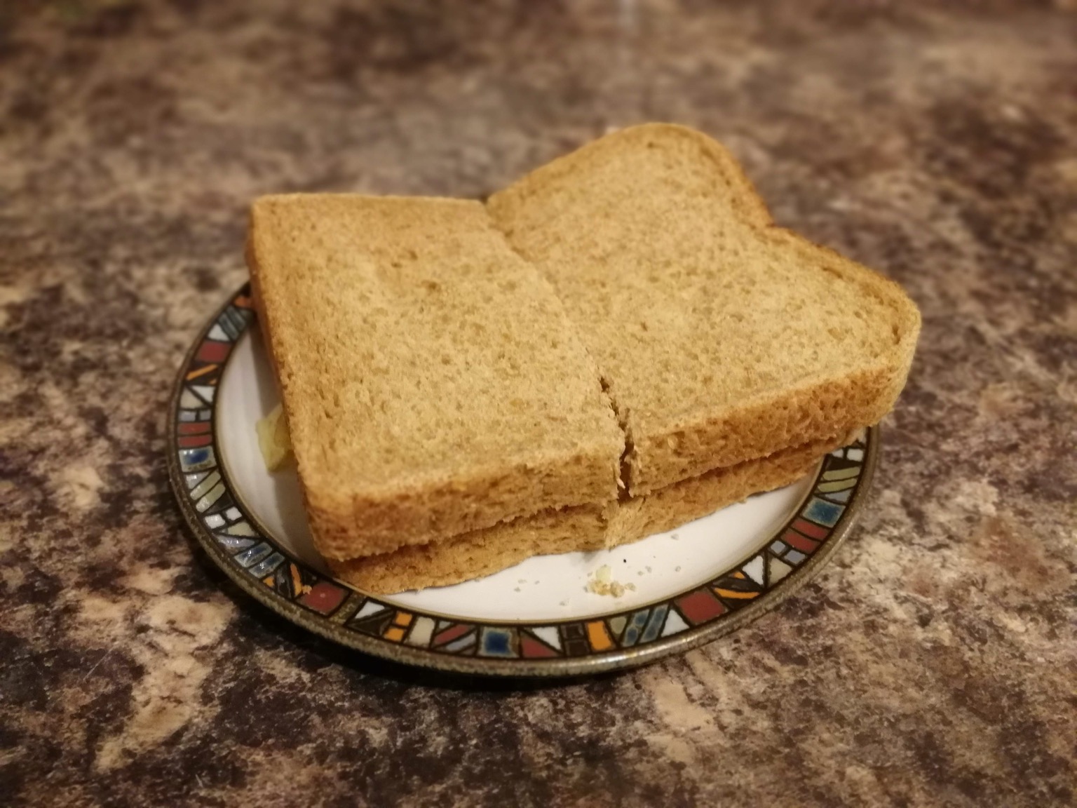 Halved brown crisp sandwich on a plate on granite