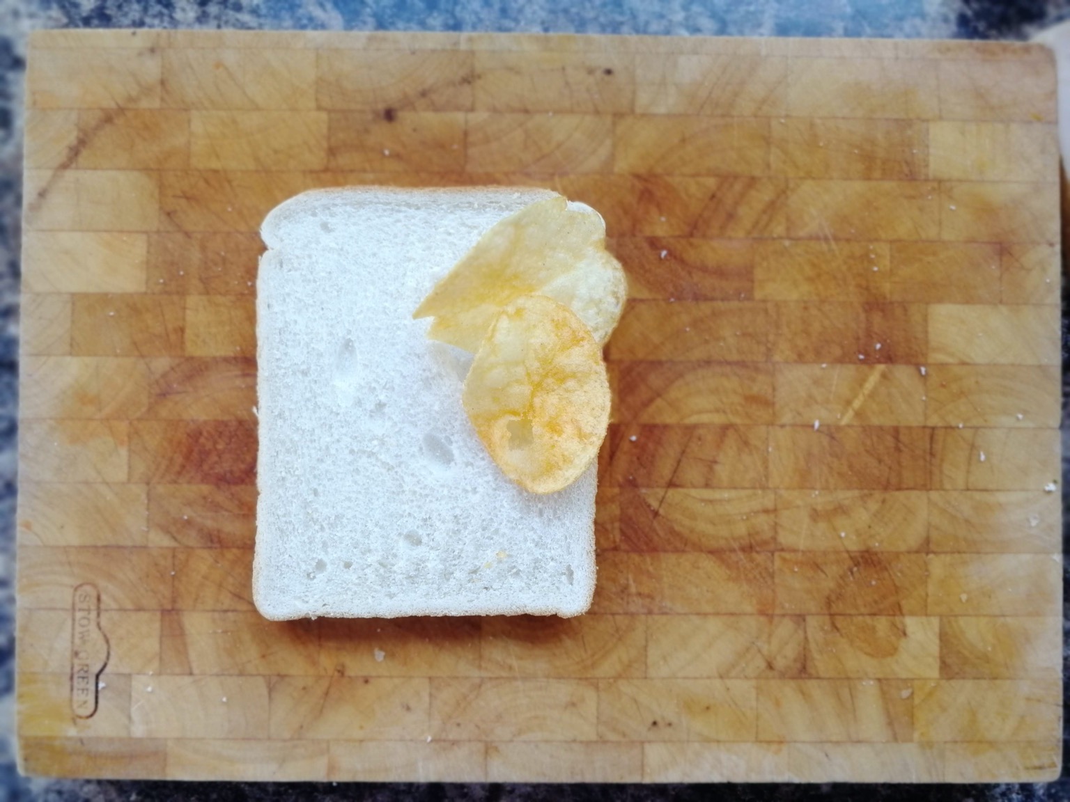 Two crisps on white bread on a chopping board
