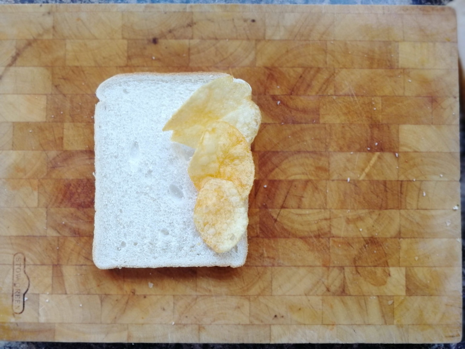 Three crisps on white bread on a chopping board