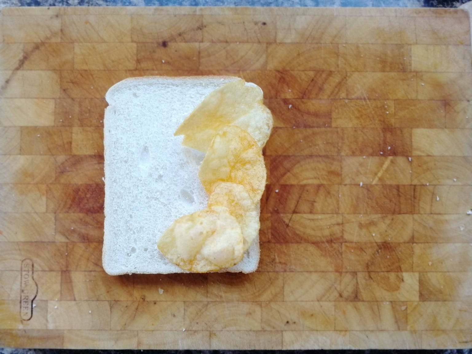 Four crisps on white bread on a chopping board