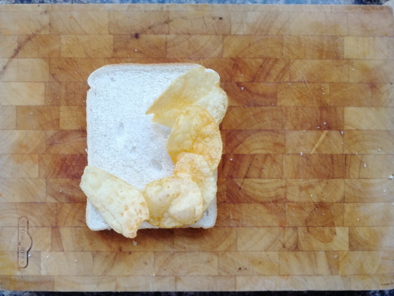 Five crisps on white bread on a chopping board