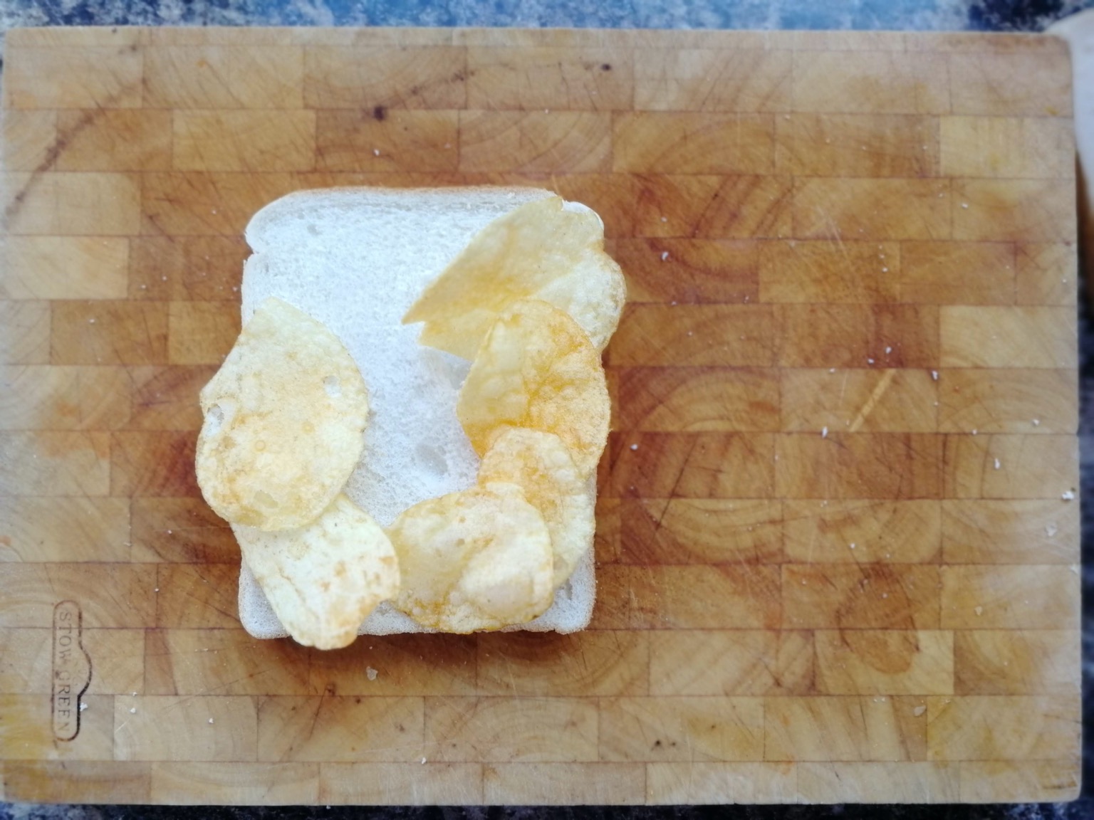 Six crisps on white bread on a chopping board