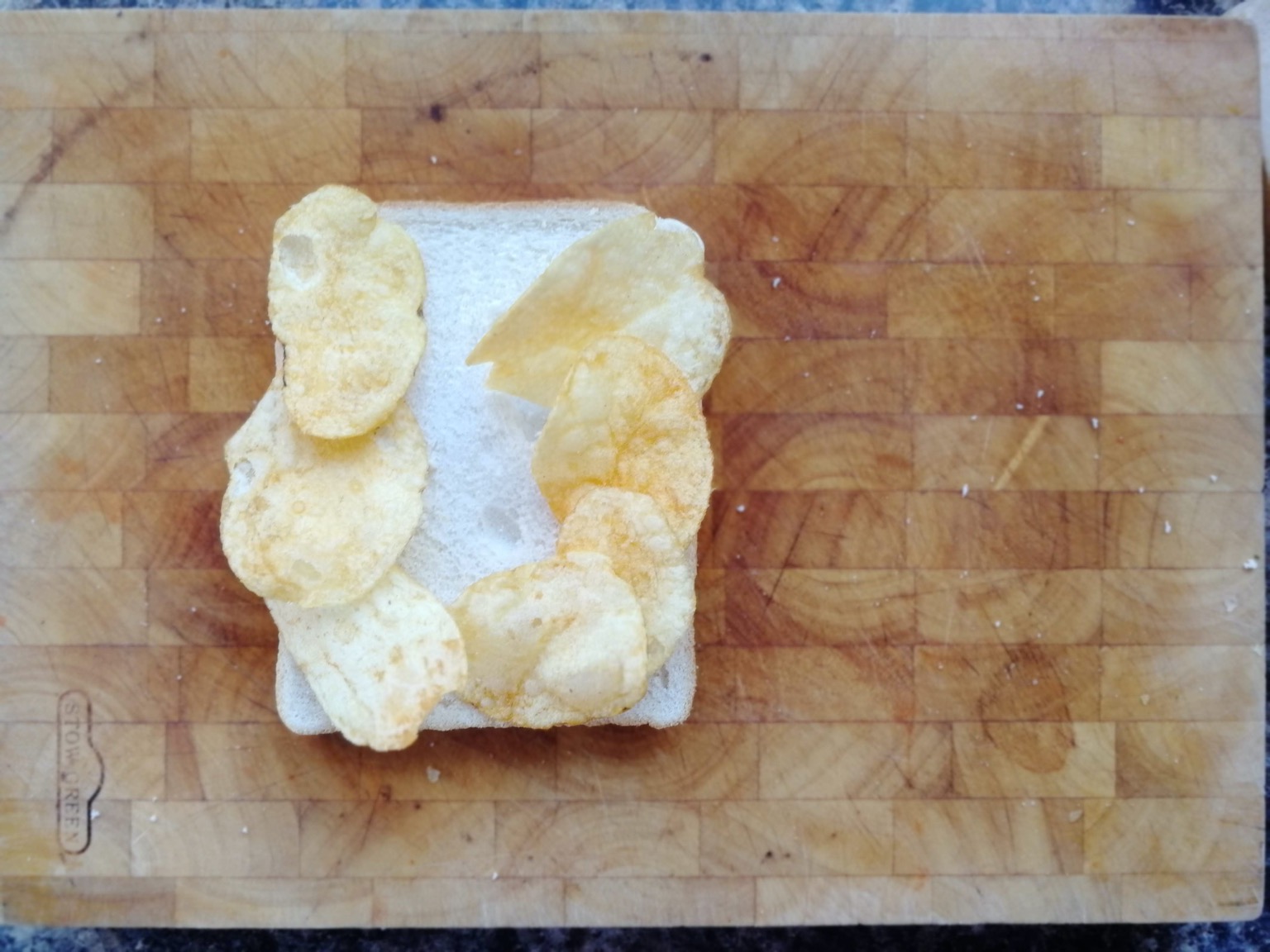 Seven crisps on white bread on a chopping board