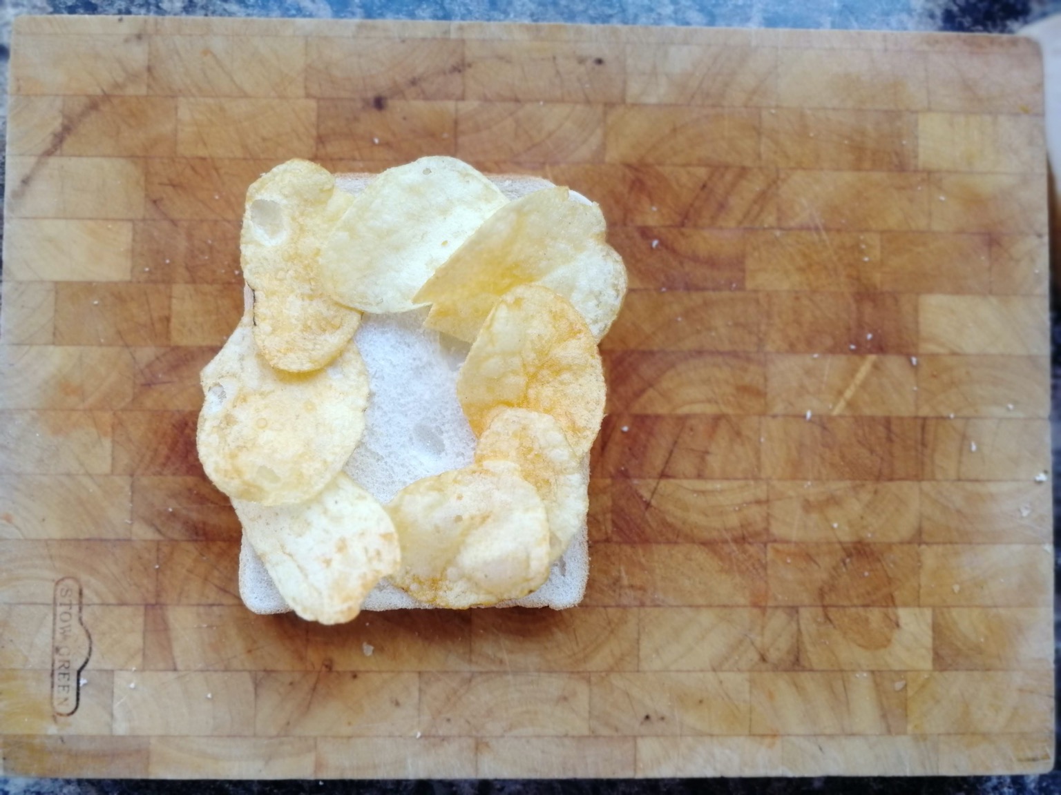 Eight crisps on white bread on a chopping board