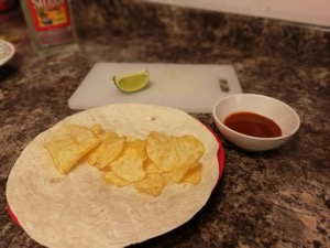 Crisps on an open wrap alongside lime and sauce