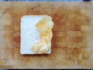 Four crisps on white bread on a chopping board