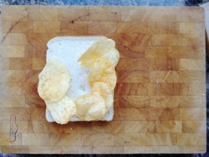 Six crisps on white bread on a chopping board