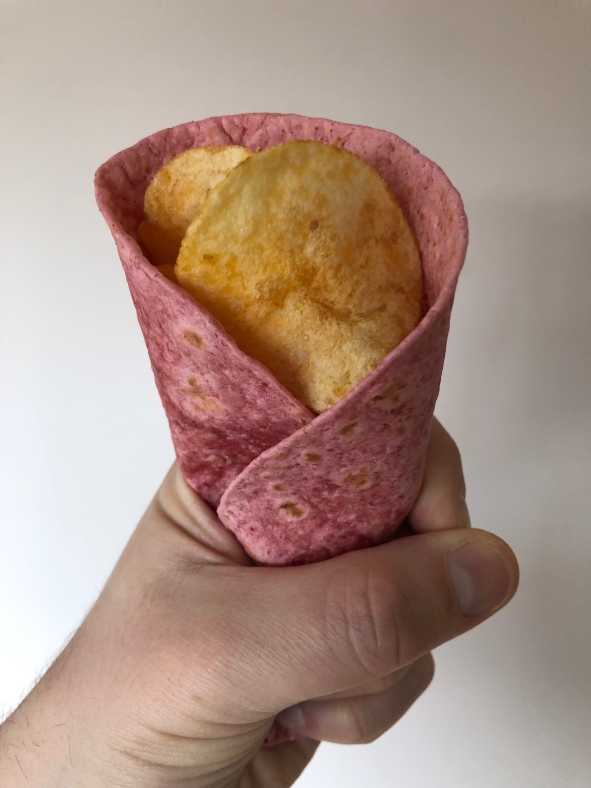 Potato crisps held in a pink tortilla wrap