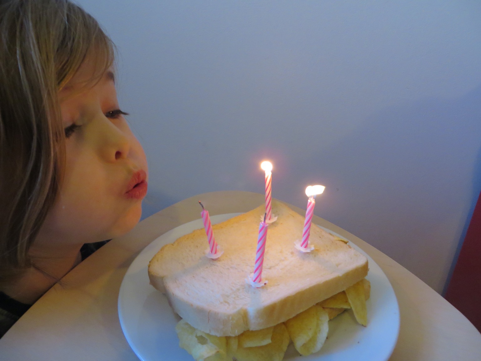 Child blowing out four candles on a crisp sandwich