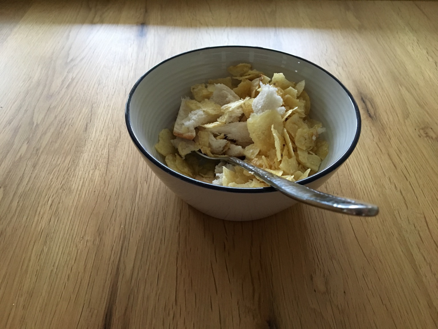 Torn white bread and crisps in a bowl with a spoon